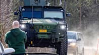 Large green military vehicle seen from the front, driving on a dusty country road.