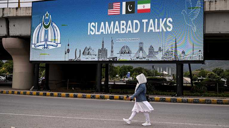 A civilian walks down the street past a large illuminated sign that reads Islamabad Talks.