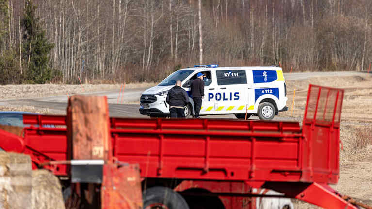 Ihmisiä poliisiauton luona hiekkatiellä pellon vieressä.