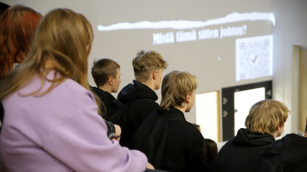 Sysmän yhteiskoulun koululaisia kuuntelemassa luentoa koulun portaikossa istuen, kasvot poispäin.