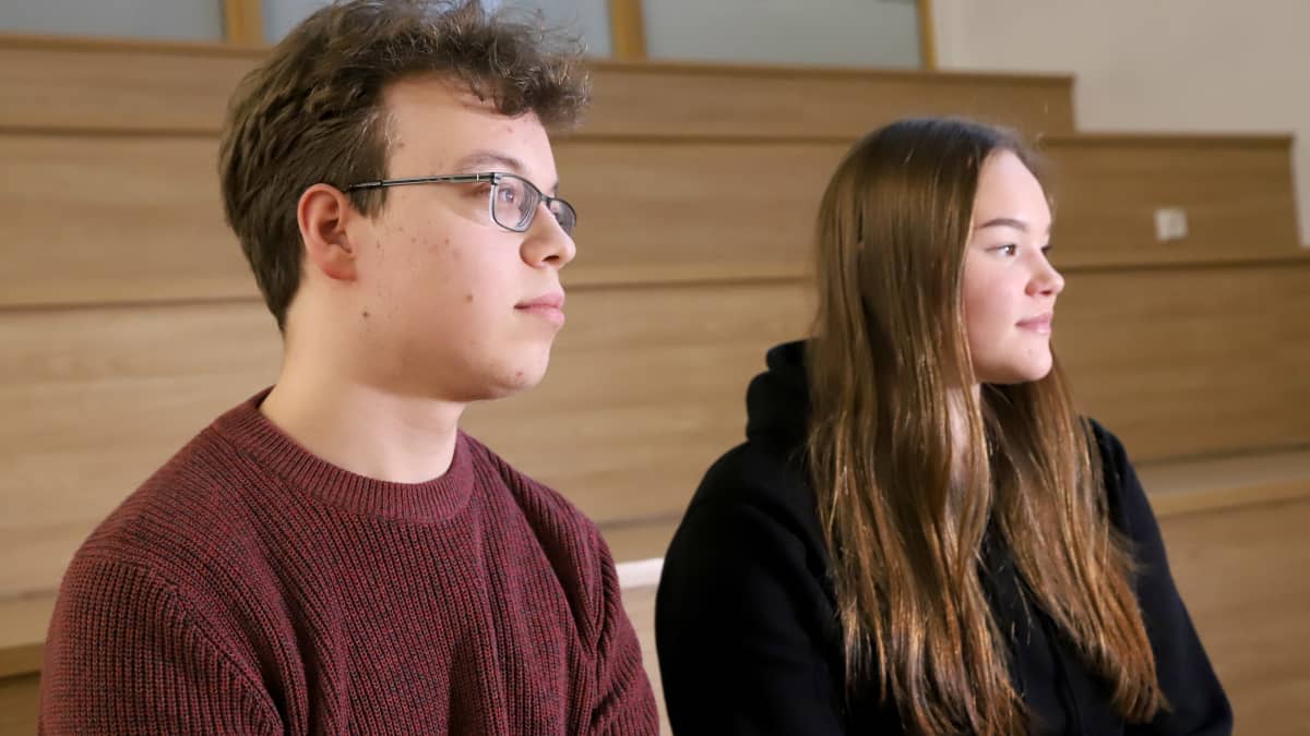 Sysmän yhteiskoulun lukion oppilaat Kia Alanne ja Lauri Hildén istuvat vierekkäin koulun sisällä portailla, katsovat sivusuuntaan kamerasta. 
