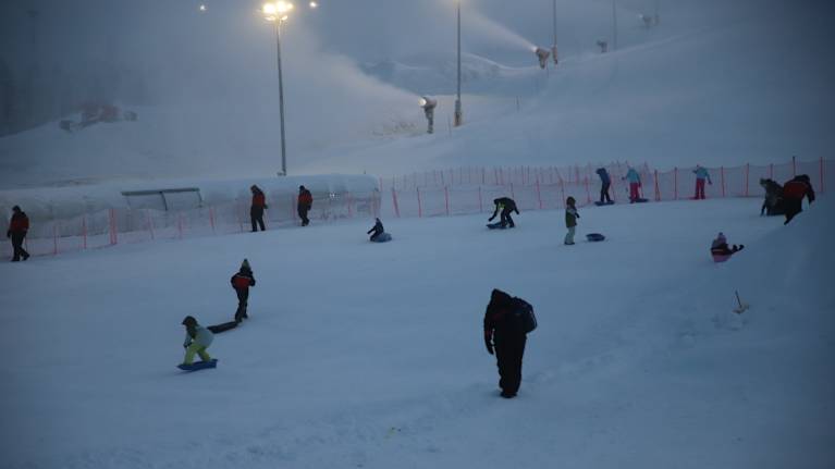Winter landscape with people enjoying sledding on a snowy slope. 