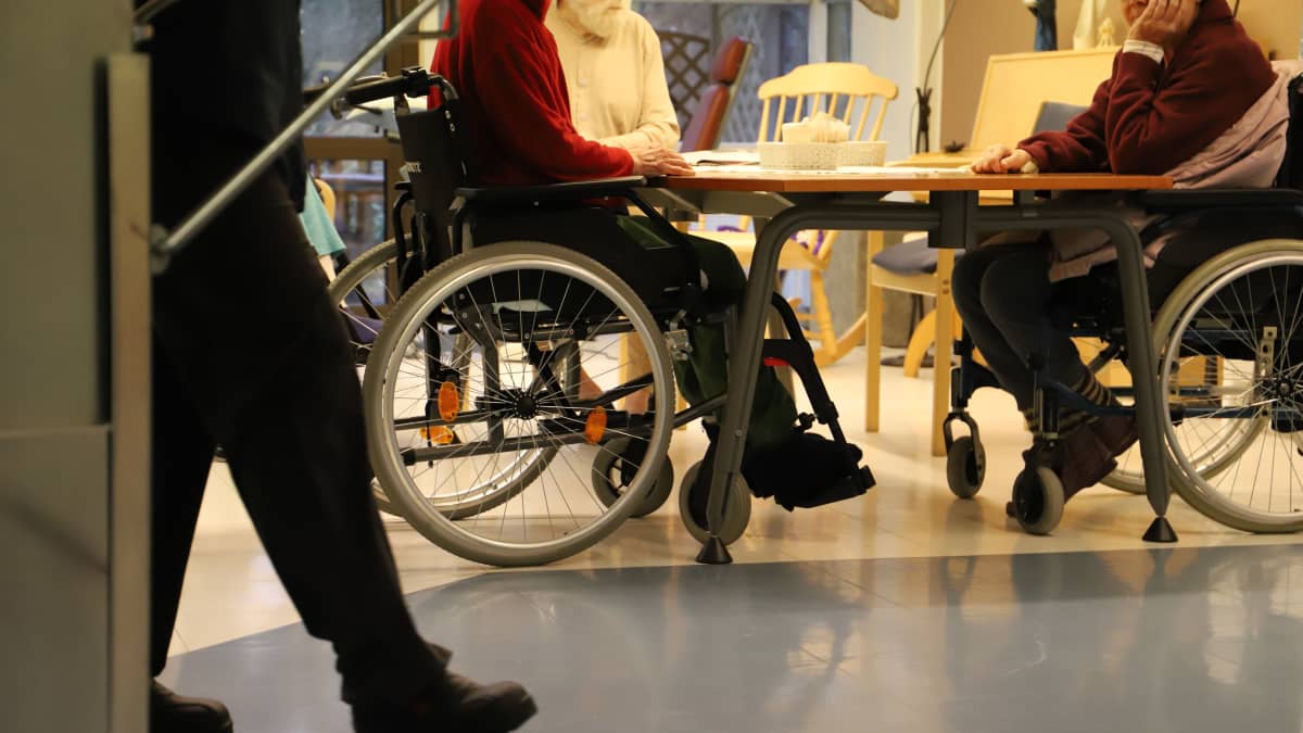 Två rullstolsburna personer sitter vid ett matbord.