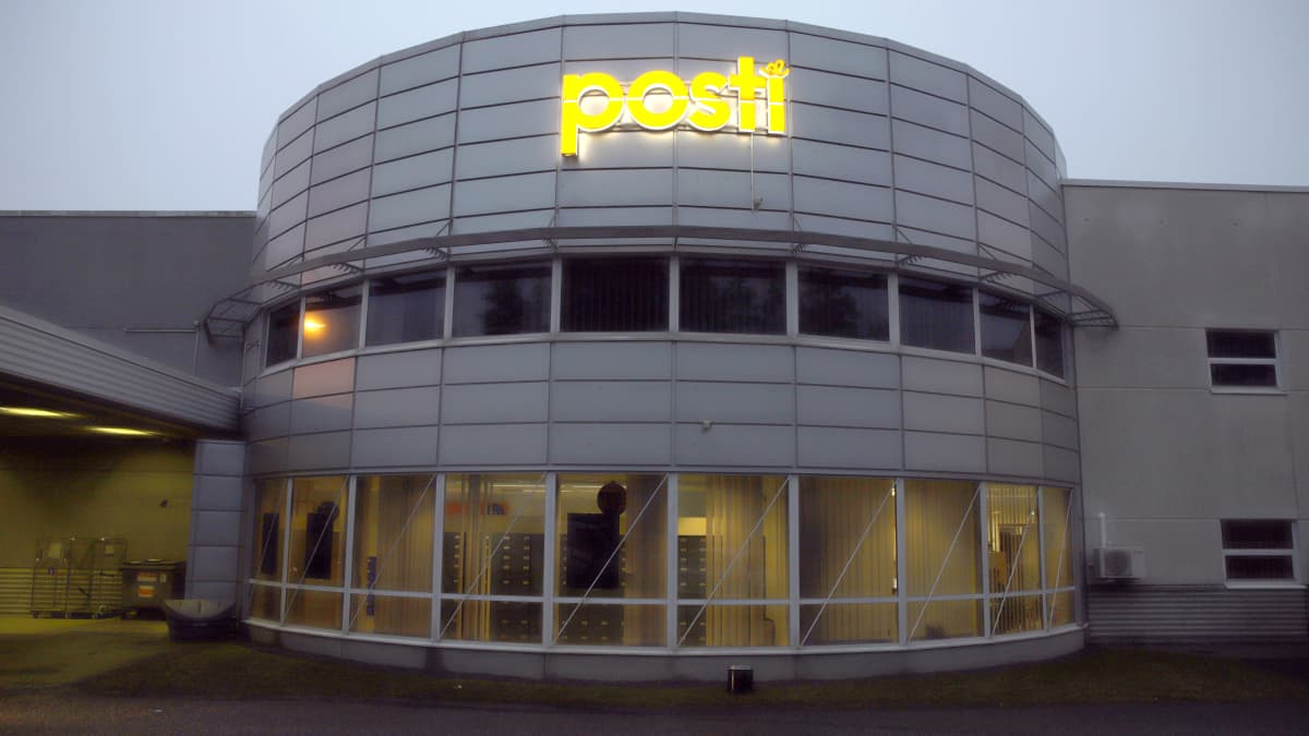 A rounded building with a metal facade and an orange neon sign reading Posti.