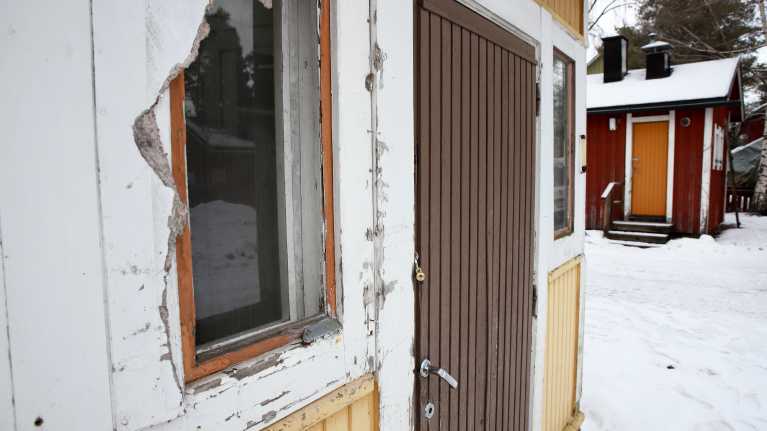 keltaisen omakotitalon kuistin ikkunassa repeytynyt peitelevy