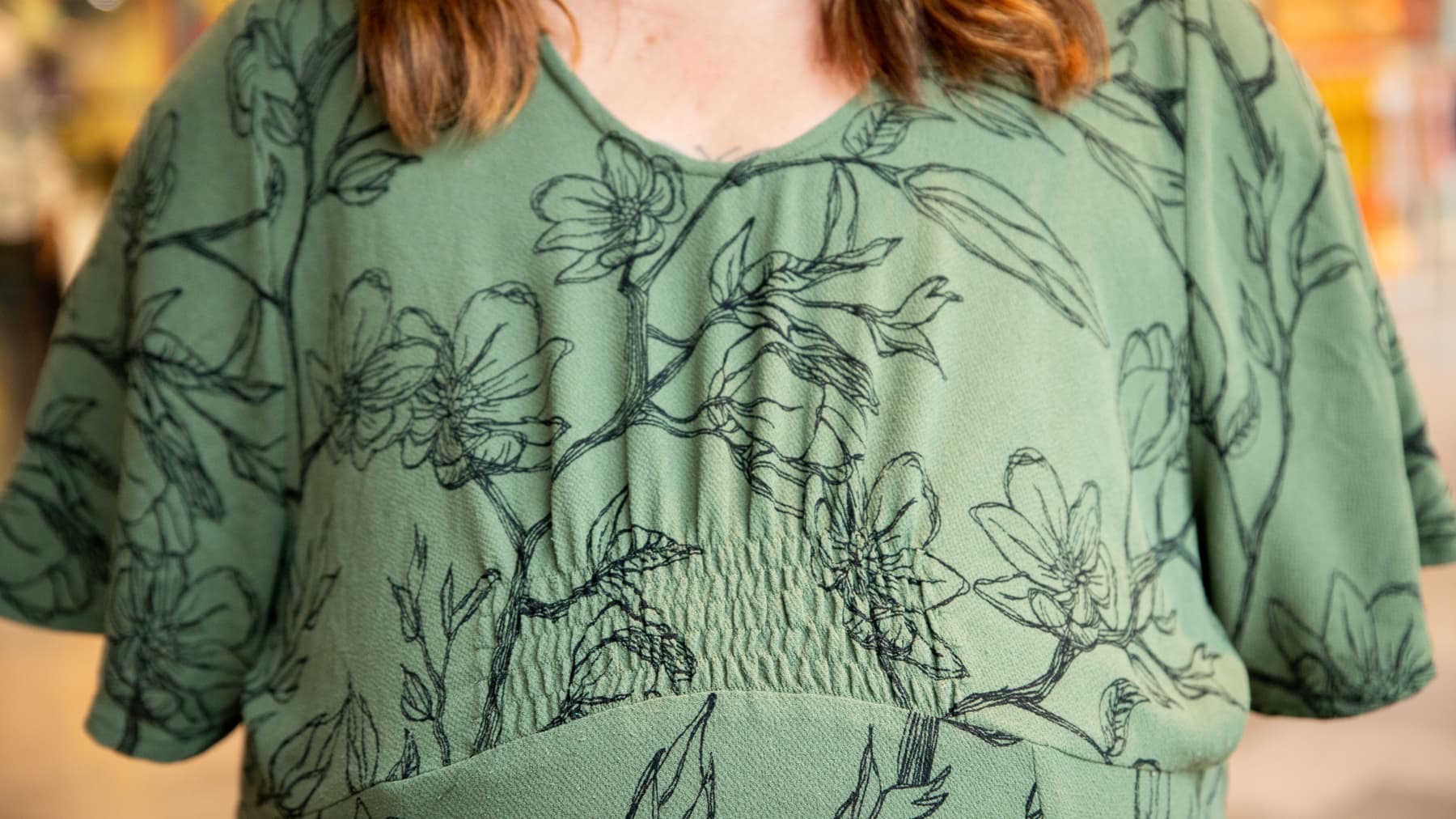 Kirsi Laine seisoo kameran edessä. Hänellä on yllään vihreä mekko, jossa mustaa kuviota. Kirsin rinnat on leikattu viisi vuotta sitten pois syövän vuoksi.
