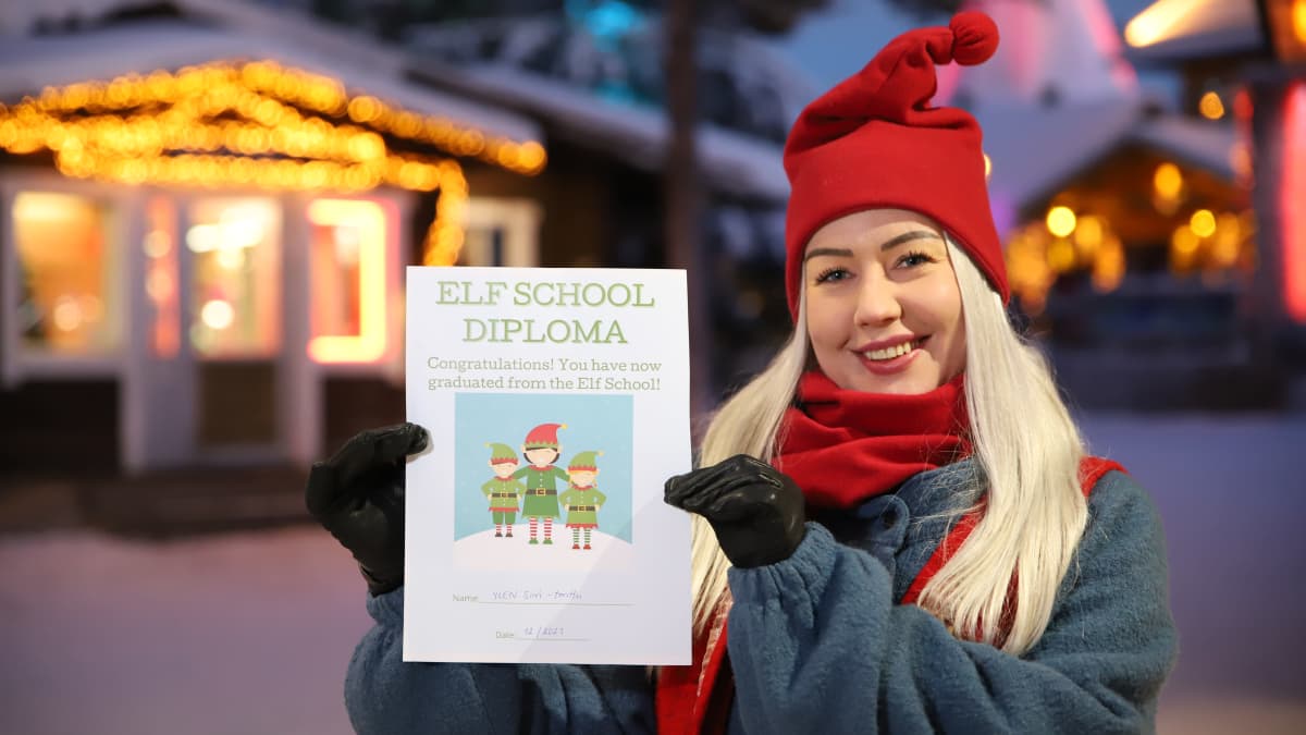 Tonttu Minna Tuomenharju pitää käsissään Tonttukoulun diplomia ja näyttää sitä kameralle. 