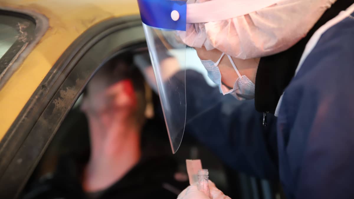 Suojavarusteisiin sonnustautunut sairaanhoitaja ottaa näytettä autossa istuvan henkilön nenästä koronatestipisteellä.