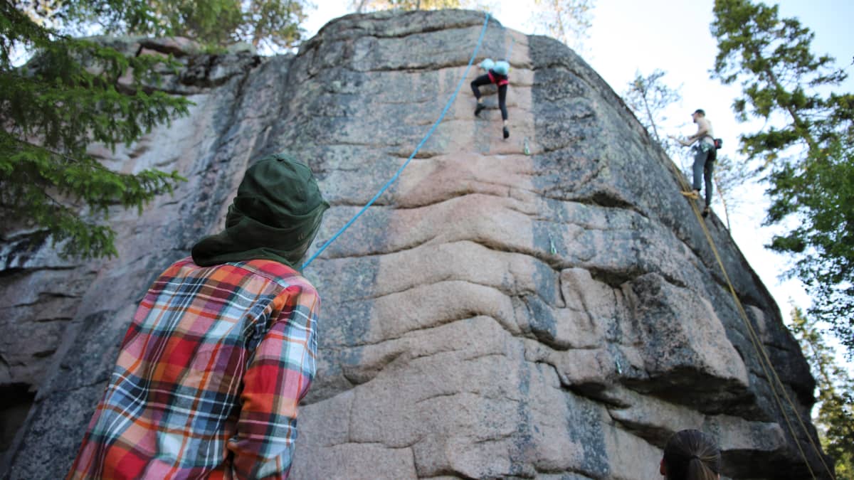 Ruutupaitainen Antti Antikainen varmistaa köyden kanssa, kun turkoosipaitainen tytär Pinja kiipeää korkealla kallioseinämällä.