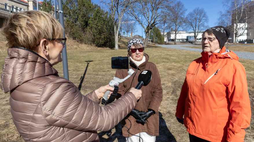 Toimittaja kuvaa ja haastattelee kahta naista puistossa.