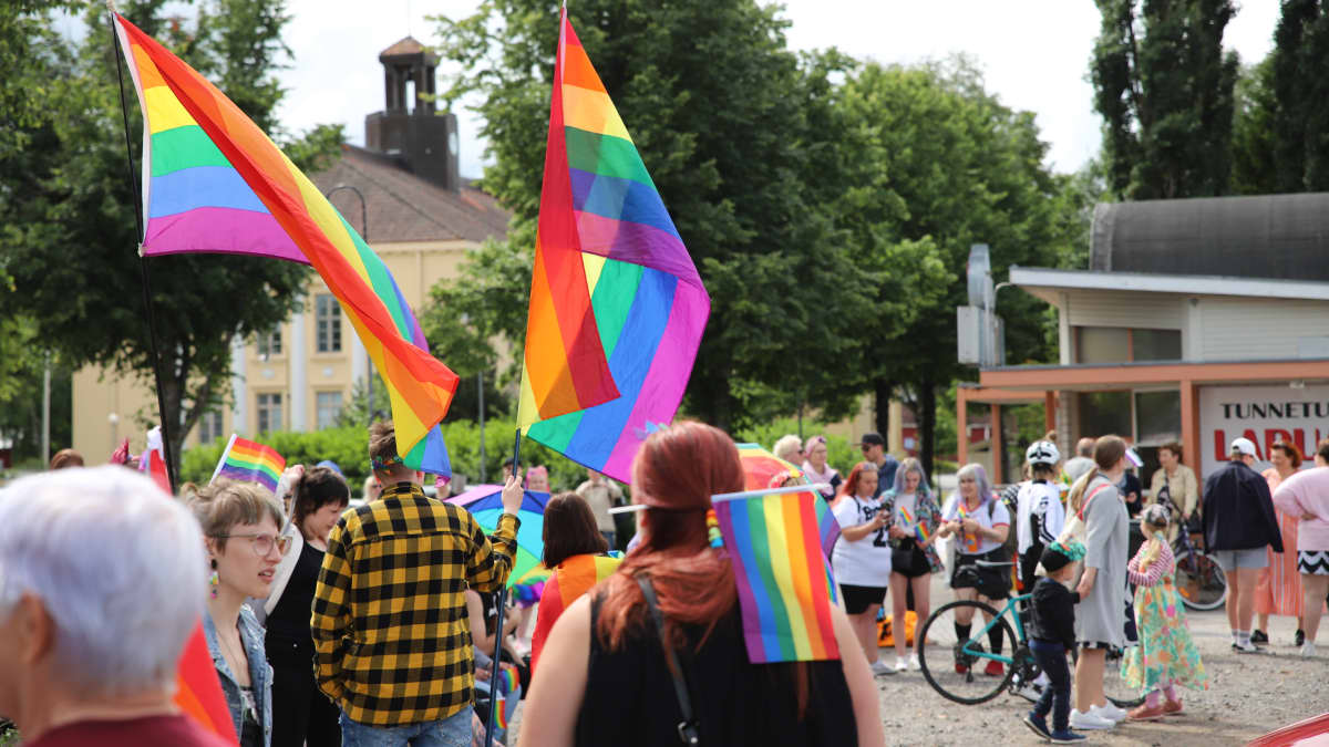 Pride-tapahtumassa liikkuvia ihmisiä Lapualla aurinkoisena kesäisenä päivänä, kuvissa näkyy sateenkaarilippuja.