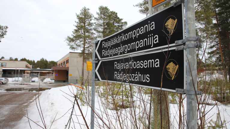 Kuvassa Ivalon Rajajääkärikomppanian ja Rajavartioaseman kyltit, taustalla rakennuksia.