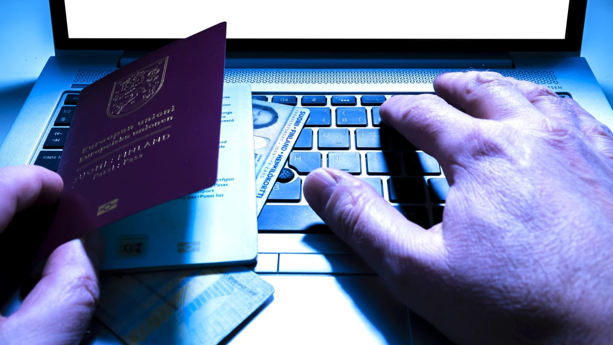Miehen kädet sekä passi ja henkilöllisyystodistuksia tietokoneen näppäimistöllä.