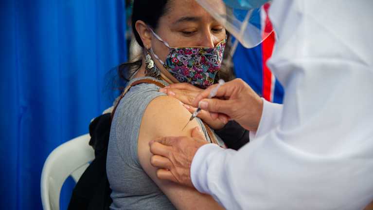 En kvinna i munskydd får coronavirusvaccin.