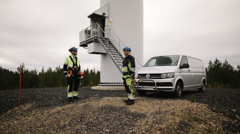 Tuulivoima-asentaj aTeemu Jacklin ja johtava tuulivoima-asentaja Joonas Simola seisovat tuulivoimalan edustalla pakettiauton edessä.
