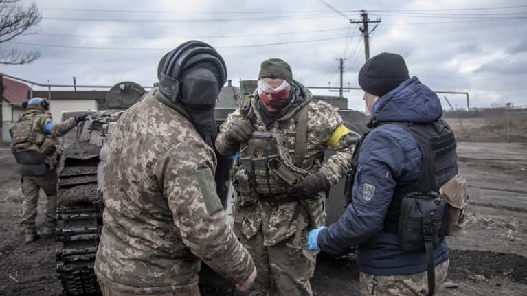 Ukrainalaissotilas verinen kääre kasvoillaan kahden muun sotilaan keskellä.