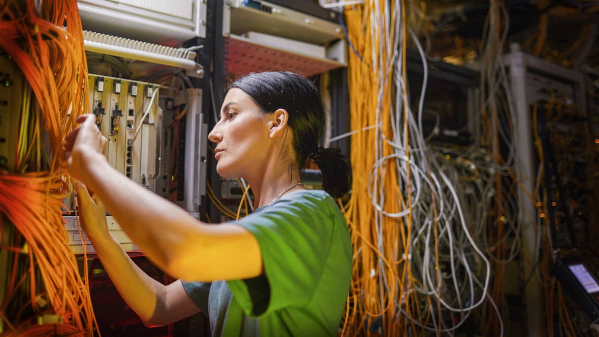 En elektriker står och jobbar vid ett elbås med en massa kablar.