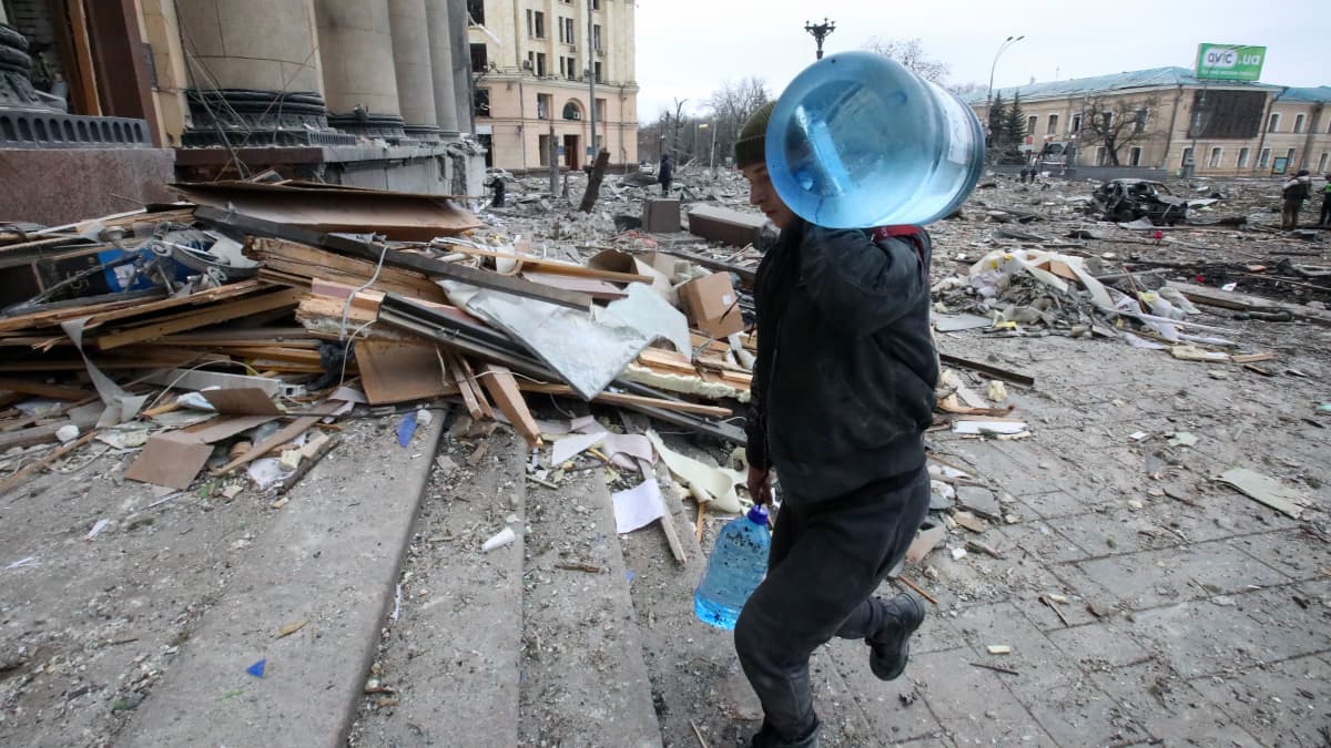 Mies kantaa vesipulloja Harkovassa pommitustuhojen keskellä.