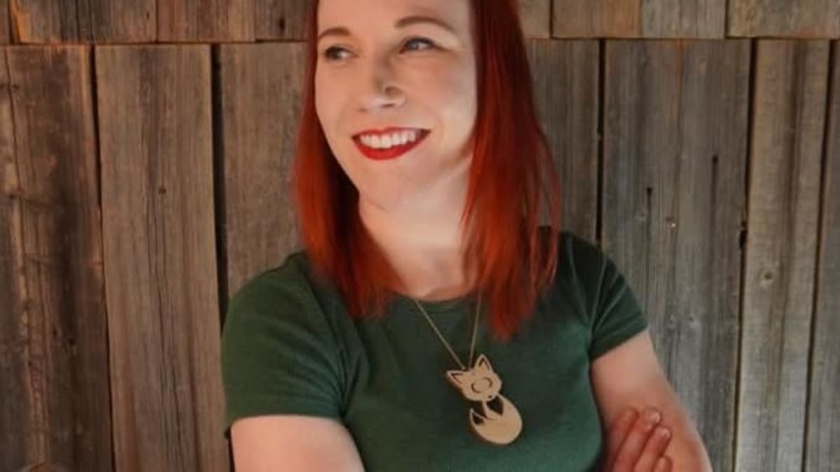Johanna Rita seisoo hymyillen kädet supussa puuseinää vasten