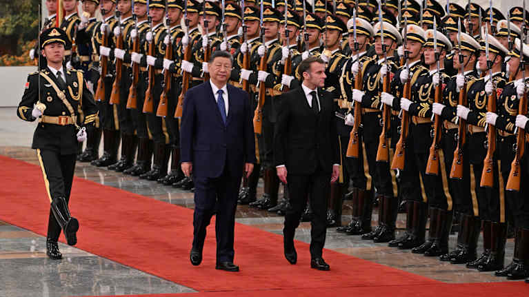 Xi Jinping ja Emmanuel Macron kävelevät vierekkäin tummat puvut päällään punaista mattoa pitkin Kiinan kunniakompanian läpi.