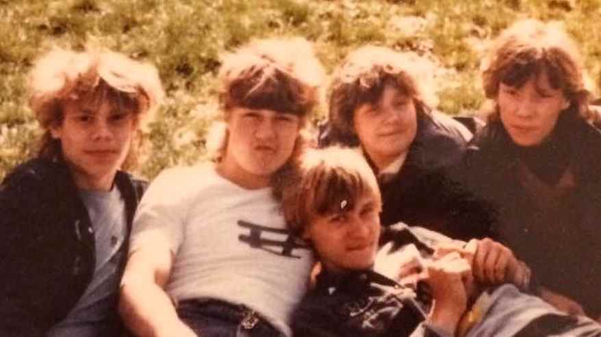 Viisi teinipoikaa 1980-luvun pilottitakeissa ja takatukkahiuksissa nurmikolla kasassa. 