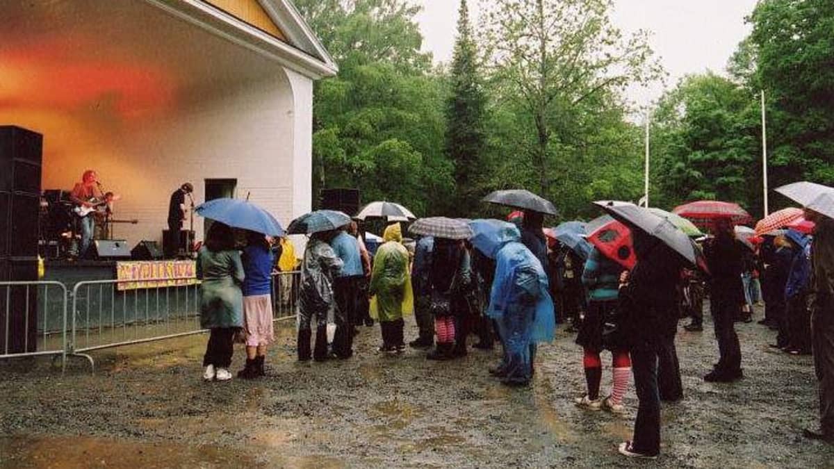 Hämeenlinnan Kaupunginpuiston esiintymislavalla Ultramariini Ämyrockissa vuonna 2004, yleisöä sateenvarjoineen kuuntelemassa.
