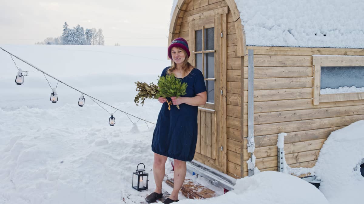 Sauna host and healer Laura Foon stands in front of her portable sauna on a snowy landscape.