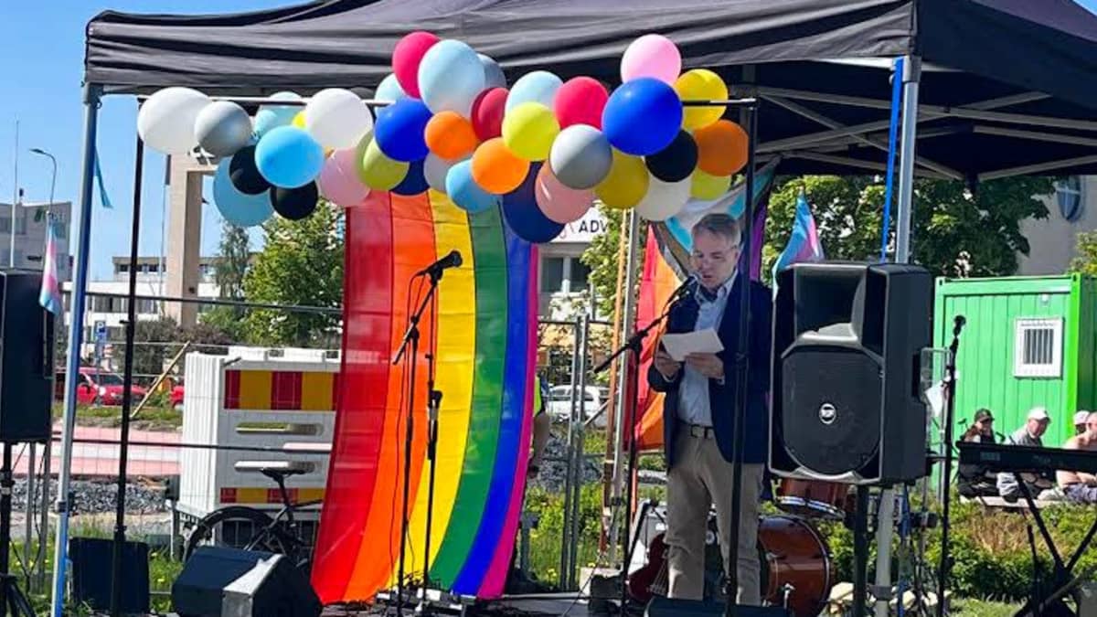 Pekka Haavisto håller tal i en paviljong med ballonger i regnbågens alla färger.