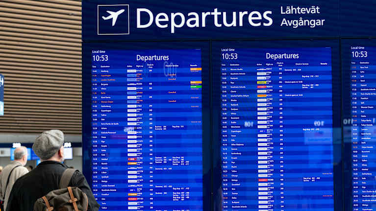 Passengers looking at a departures board at Helsinki Airport.