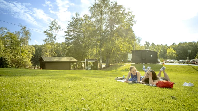 Kesäinen, vihreänä loistava kuva kahdesta nuoresta naisesta ottamassa aurinkoa nurmikolla.