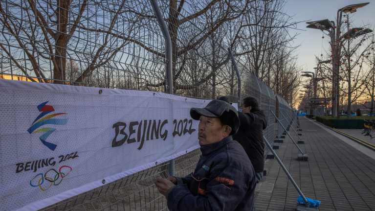 Mies kiinnittää olympiabanneria kisapaikkaa ympäröivään verkkoaitaan.