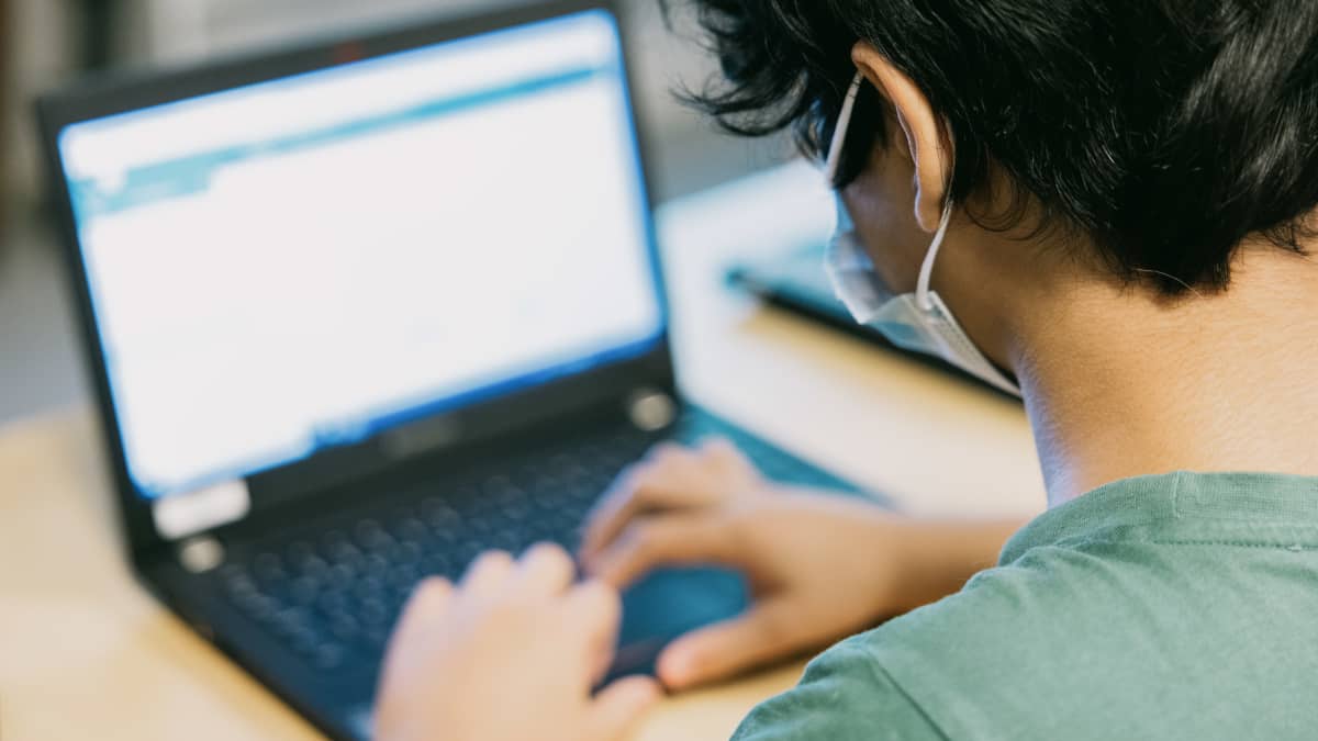 Oppilas käyttää tietokonetta kasvomaski päällään.