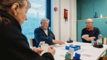 Elderly people playing a card game at a white table in senior citizens' centre.