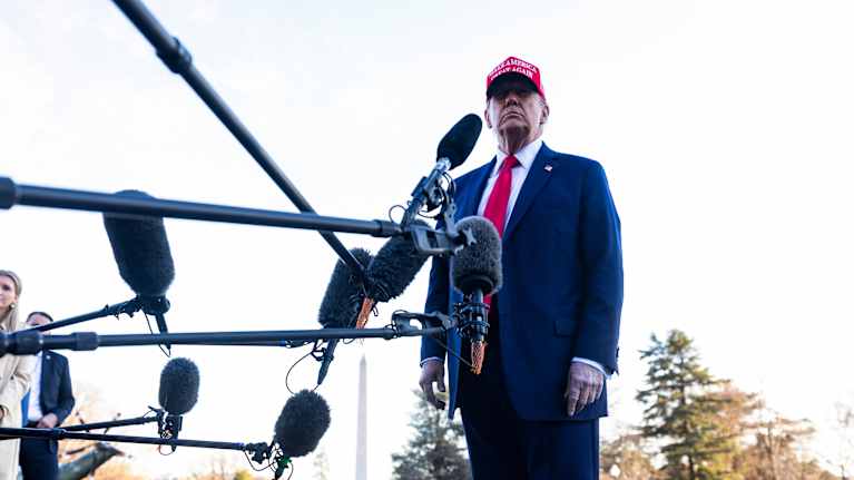 Donald Trumpov står utomhus omgiven av många mikrofoner på ställningar som pekar mot presidenten. 