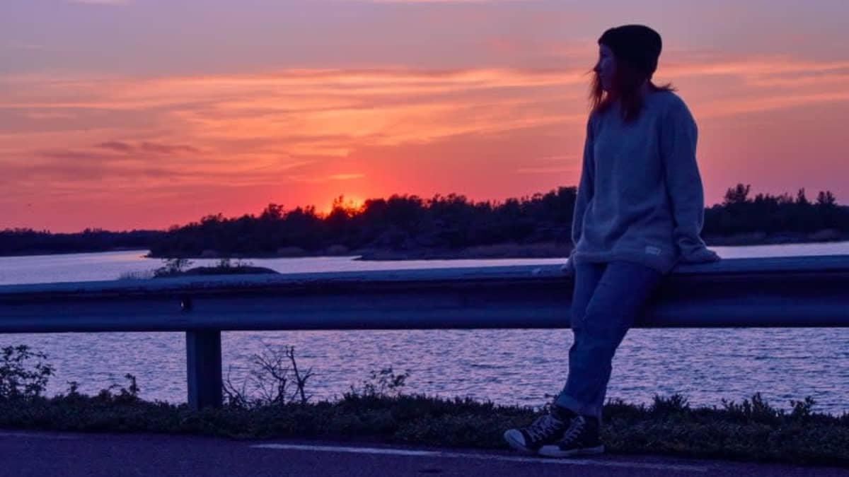 Johanna Rita nojaa autotien kaiteeseen ja katselee auringonlaskuun