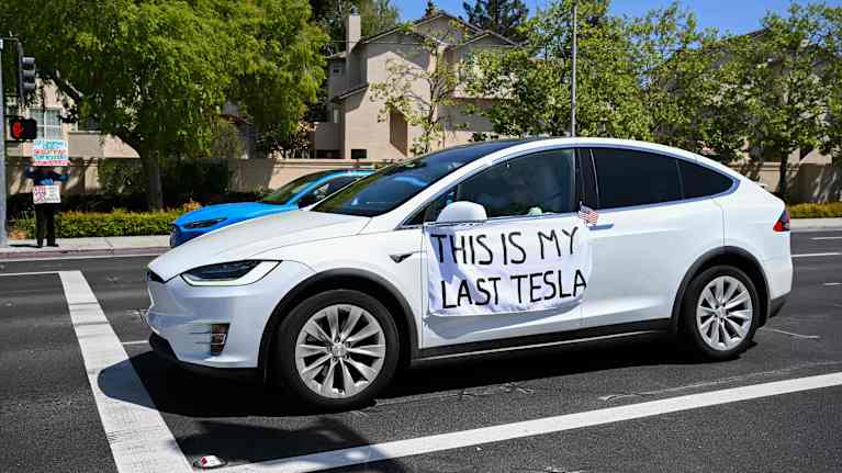En vit Teslabil på en gata med en skylt där det står " det här är min sista teslabil".