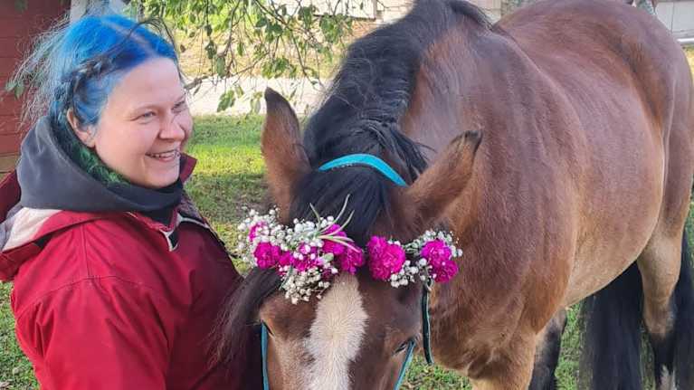 Hymyilevä nainen antaa seppelepäiselle hevoselle porkkanaa. 