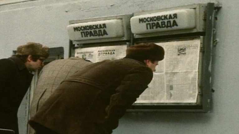 Miehet lukevat lehteä lehtitelineestä