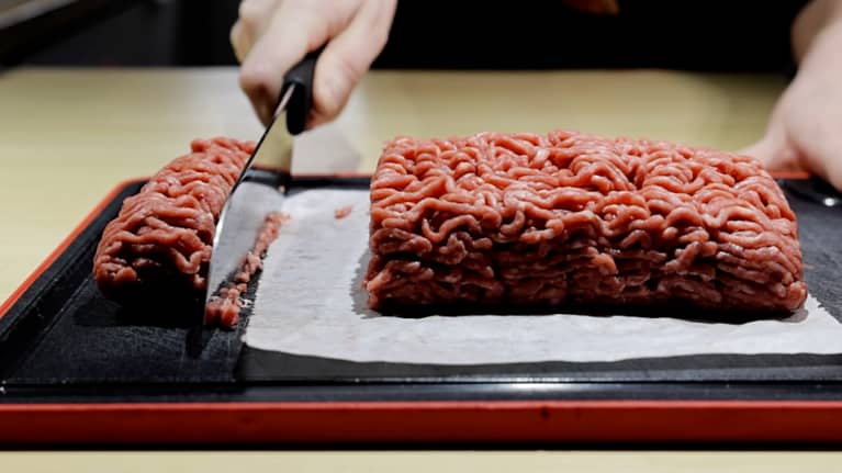 Using a butcher's knife, a hand cuts a fifth of a 500 g piece of minced meat.