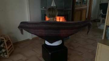 Kvinna framför en brasa med en stickad sjal på axlarna.