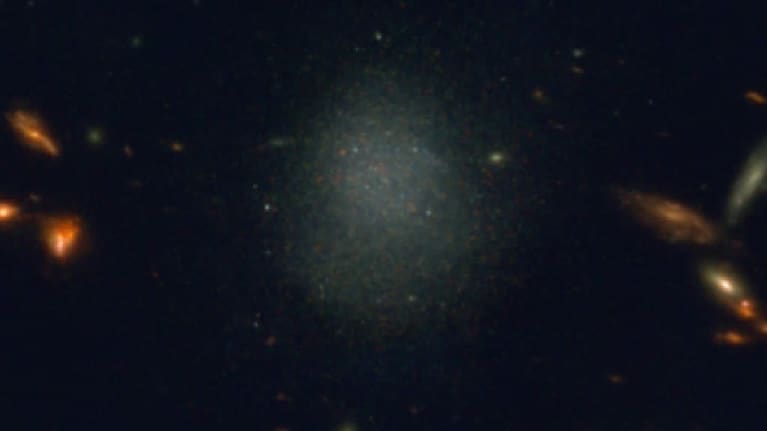 Mustassa avaruudessa näkyy sumuna pieni galaksi, josta erottuu pisteinä yksittäisiä tähtiä.