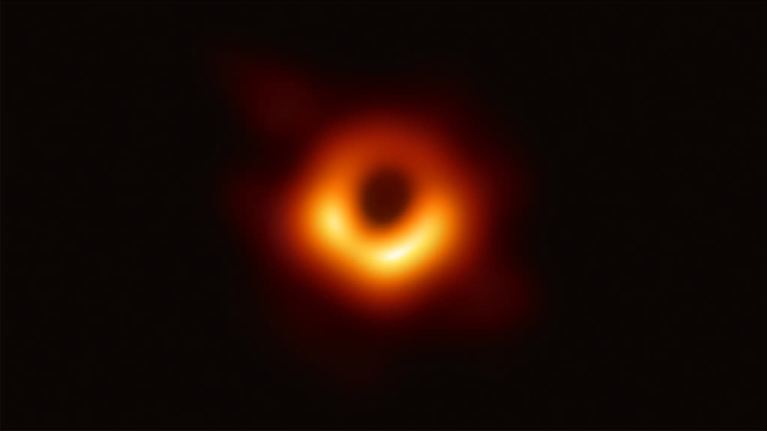 Mustan aukon pyöreä varjo ja sen ympärillä keltapunaista plasmaa. 