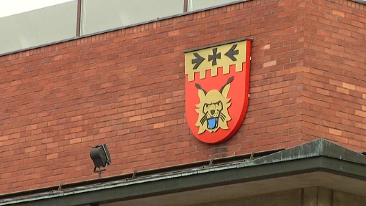 Punatiilinen seinä, johon on kiinnitetty ilvesaiheinen vaakuna.