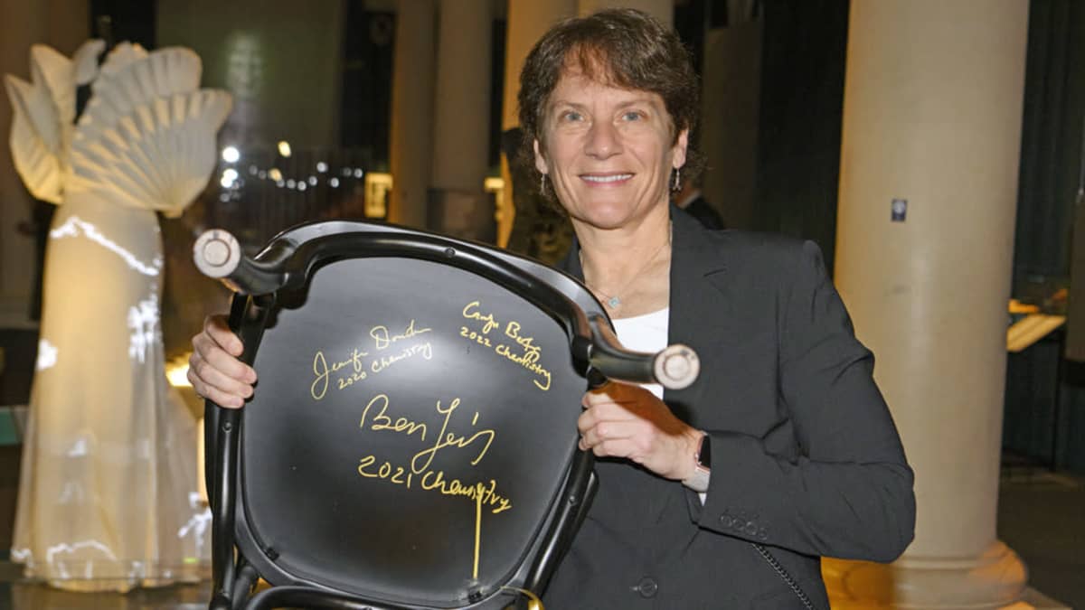Carolyn Bertozzi pitelee käsissään tuolia, jonka pohjaan hän on kirjoittanut nimensä kahden edellisen vuoden Nobel-voittajan lisäksi. 