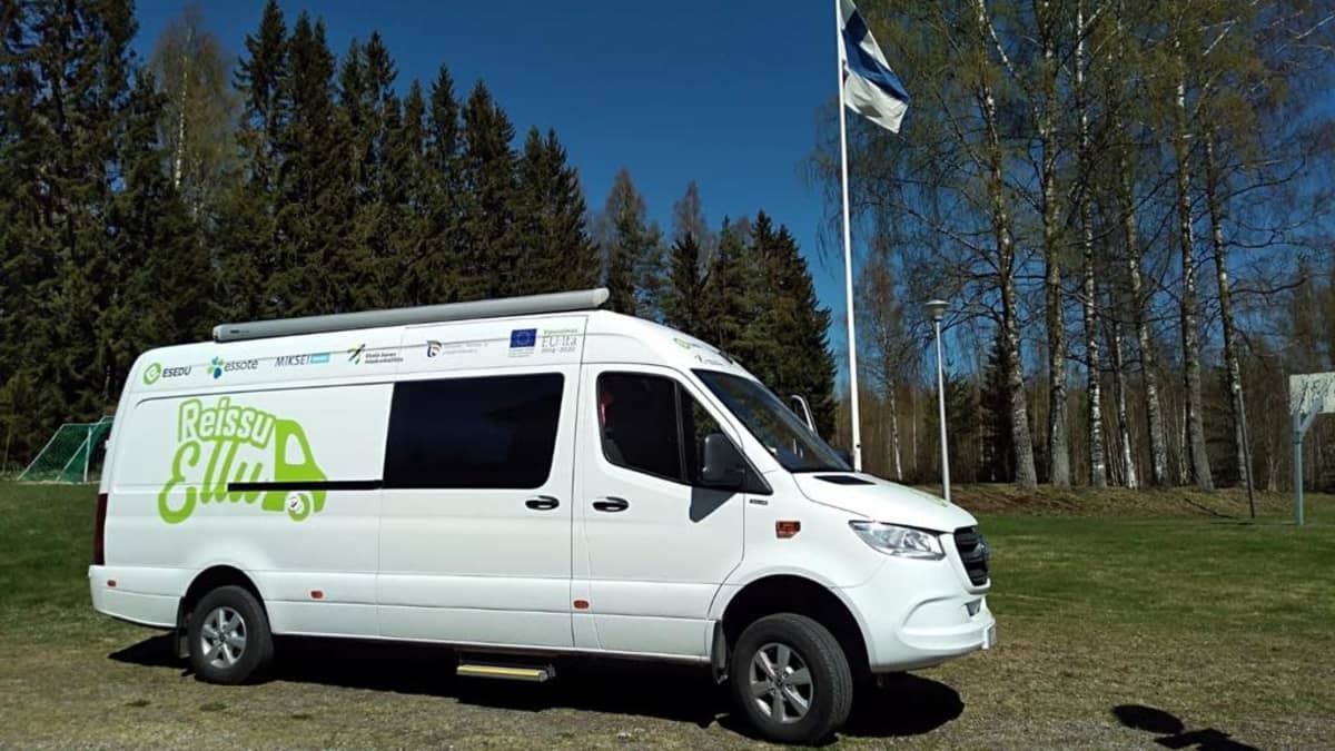 Kuvassa valkoinen pakettiauto, joka toimii Etelä-Savossa hyvinvointiautona. Kyljessä lukee vihreällä "Reissu-Ellu" eli auton nimi. Kuva on otettu keväällä.