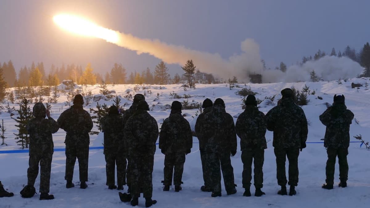 A group of conscripts stand in the snow as a projectile is fired.