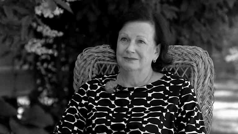 Leena Majander-Reenpää istuu korituolissa ulkona, kirja sylissään.