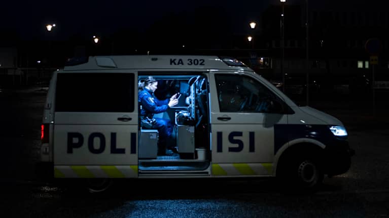 Konstaapeli istuu poliisautossa ja katsoo tablettia. 