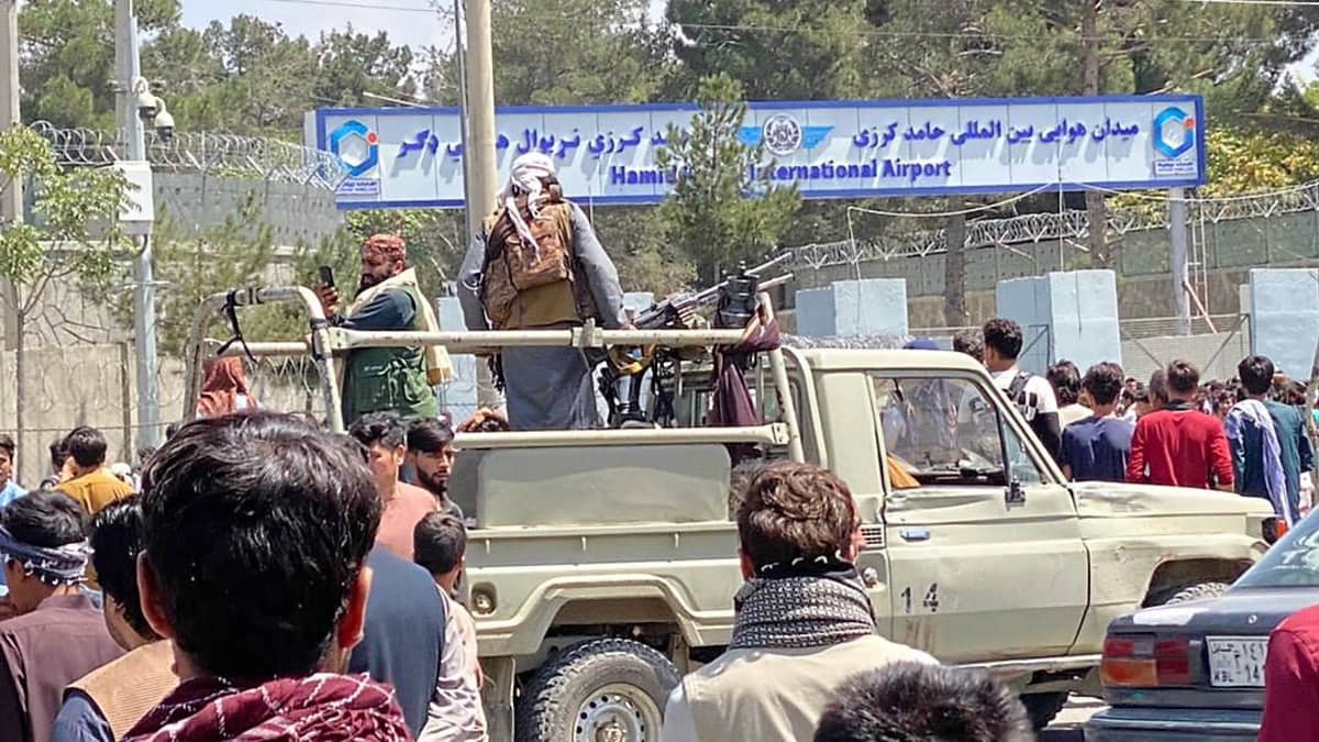 Kaksi Taliban-taistelijaa seisoo auton lavalla. Lavalle on asetettu myös konekivääri. Ympärillä seisoo ihmisiä. Taustalla näkyy lentokentän kyltti.