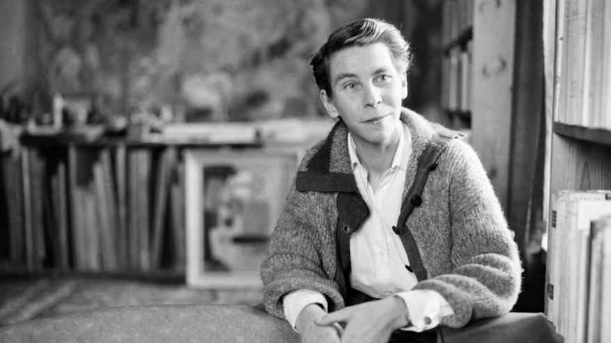 Mustavalkoisessa vanhassa valokuvassa lyhyttukkainen henkilö kauluspaidassa ja villatakissa, hymyilee, taustalla kirjahylly.